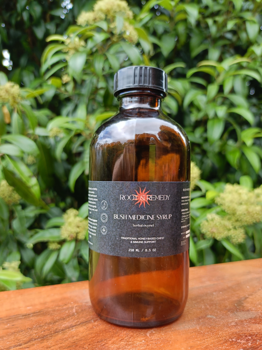 Brown bottle of Rogue Remedy Bush Medicine Syrup on a wooden surface with green foliage in the background