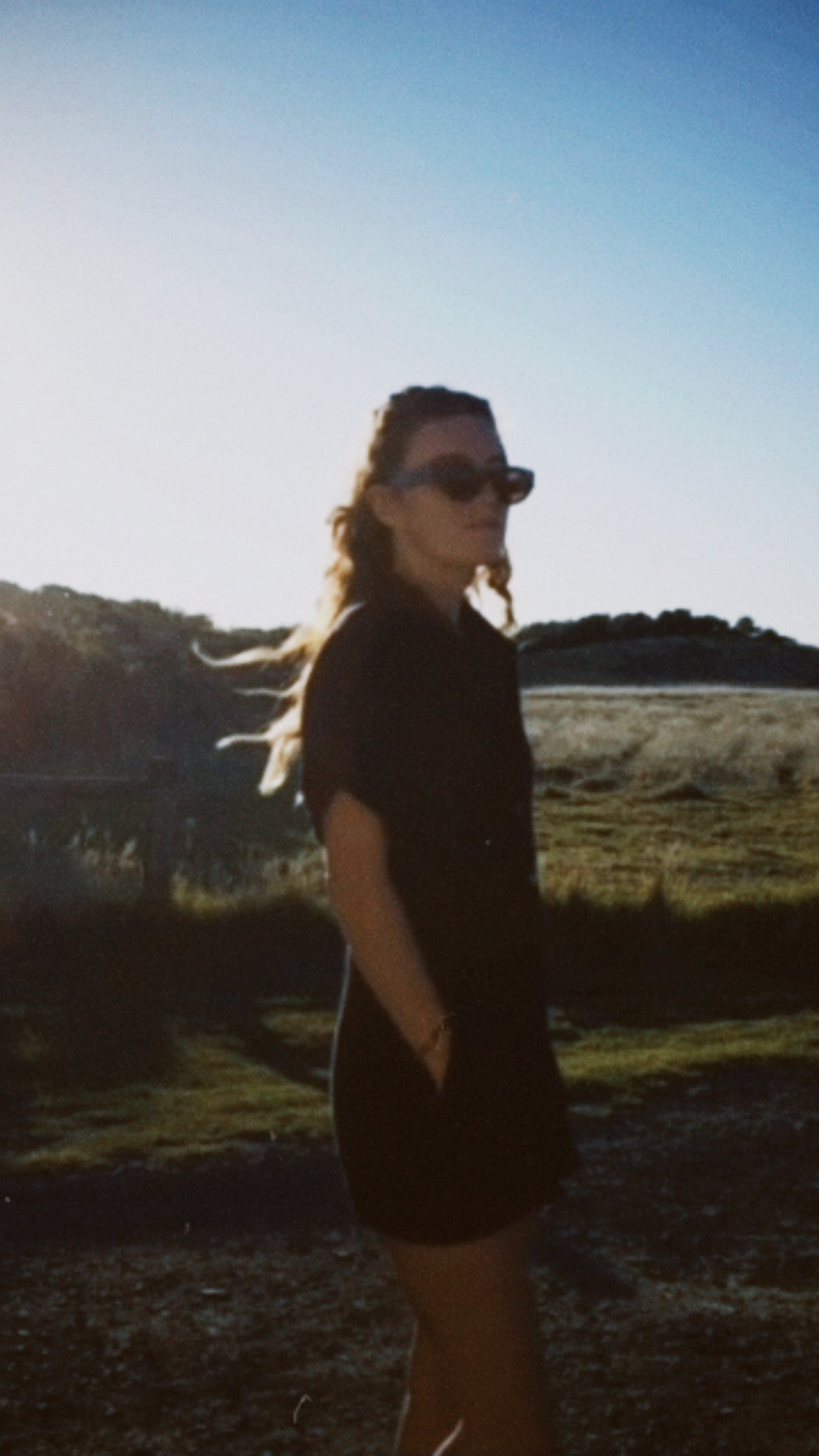 Person wearing sunglasses standing in a field with a scenic background