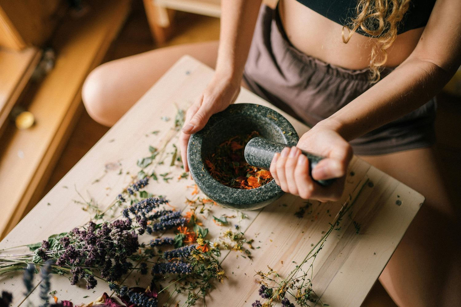 woman grinding up dried and fresh flowers in a ceramic bowl