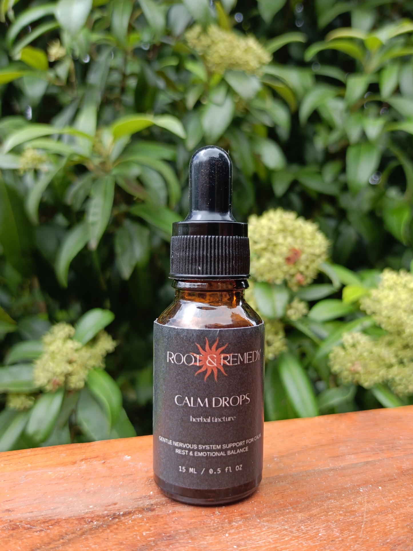 Bottle of Root & Remedy Calm Drops on a wooden surface with green foliage in the background